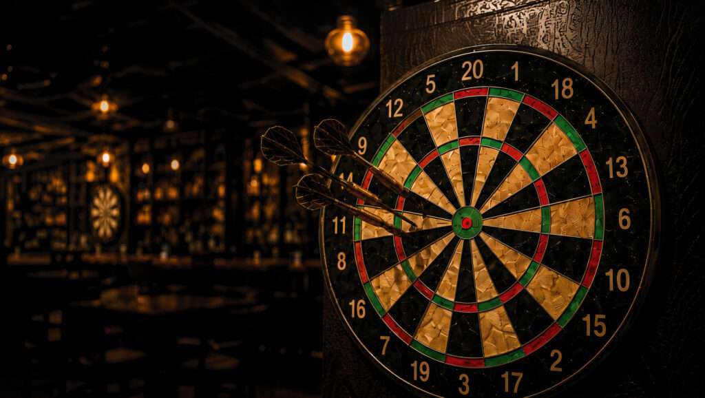 Dartscheibe mit drei Pfeilen, im Hintergrund die beleuchtete Bar